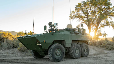 Military armored personnel carrier positioned in desert terrain at sunset with sparse vegetation