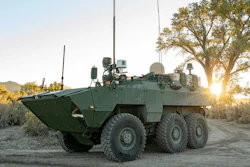 Military armored personnel carrier positioned in desert terrain at sunset with sparse vegetation
