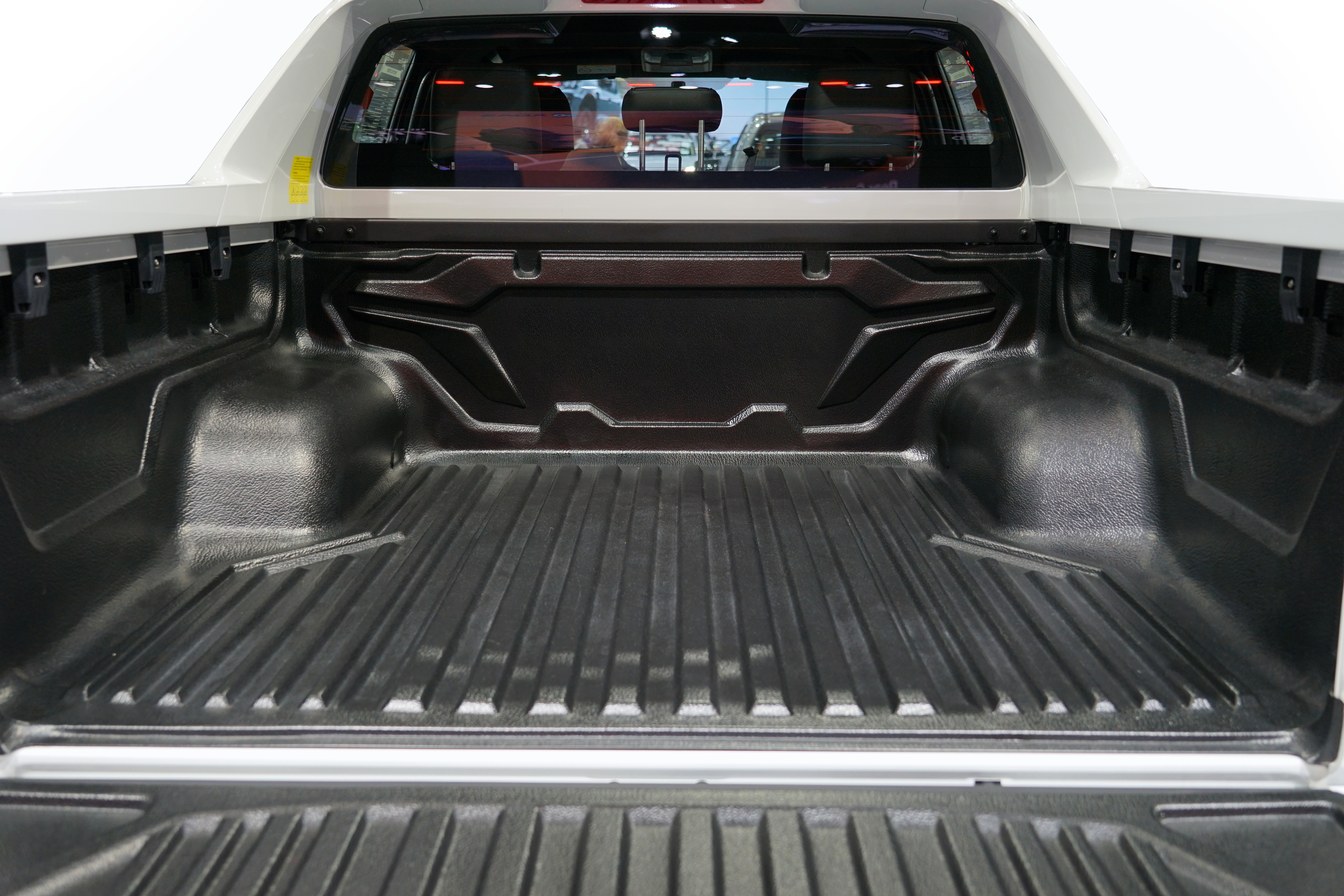 Open truck bed with textured black spray-in liner and rear window display showing road view