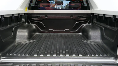 Open truck bed with textured black spray-in liner and rear window display showing road view