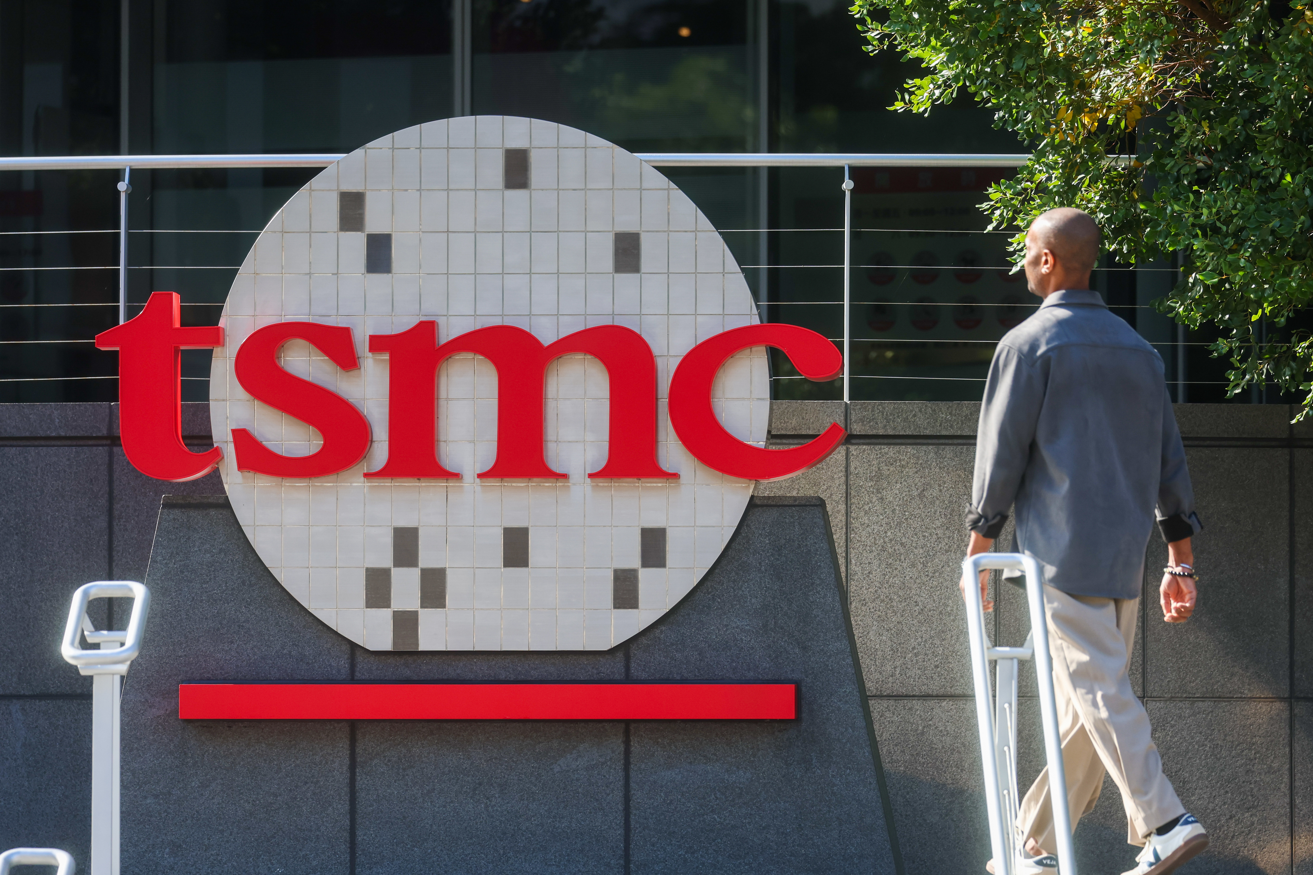TSMC logo displayed on corporate building signage with person walking past modern facility