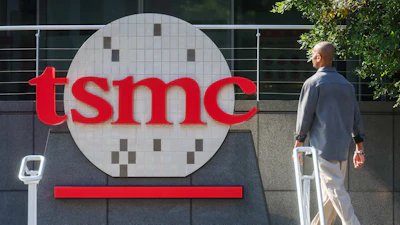 TSMC logo displayed on corporate building signage with person walking past modern facility