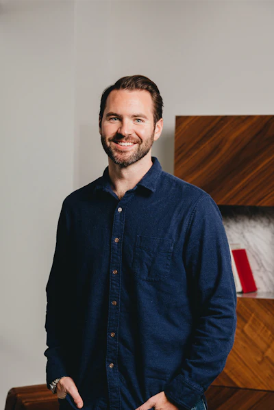 Professional portrait of a smiling man wearing a dark denim shirt in an interior setting
