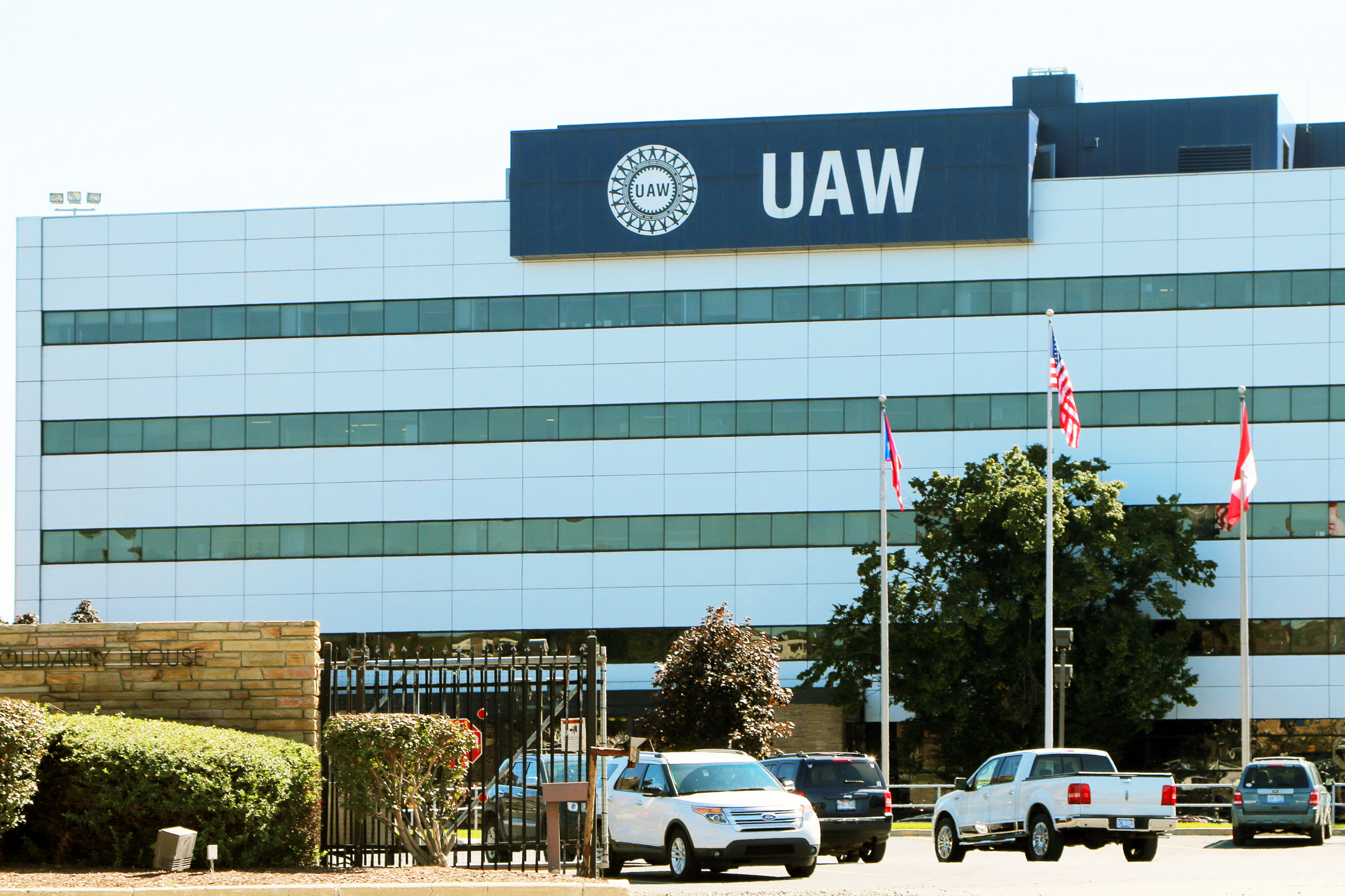 UAW headquarters building with glass facade, flagpoles, and parked vehicles in front