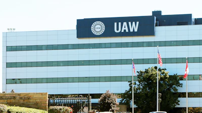 UAW headquarters building with glass facade, flagpoles, and parked vehicles in front