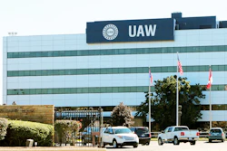 UAW headquarters building with glass facade, flagpoles, and parked vehicles in front