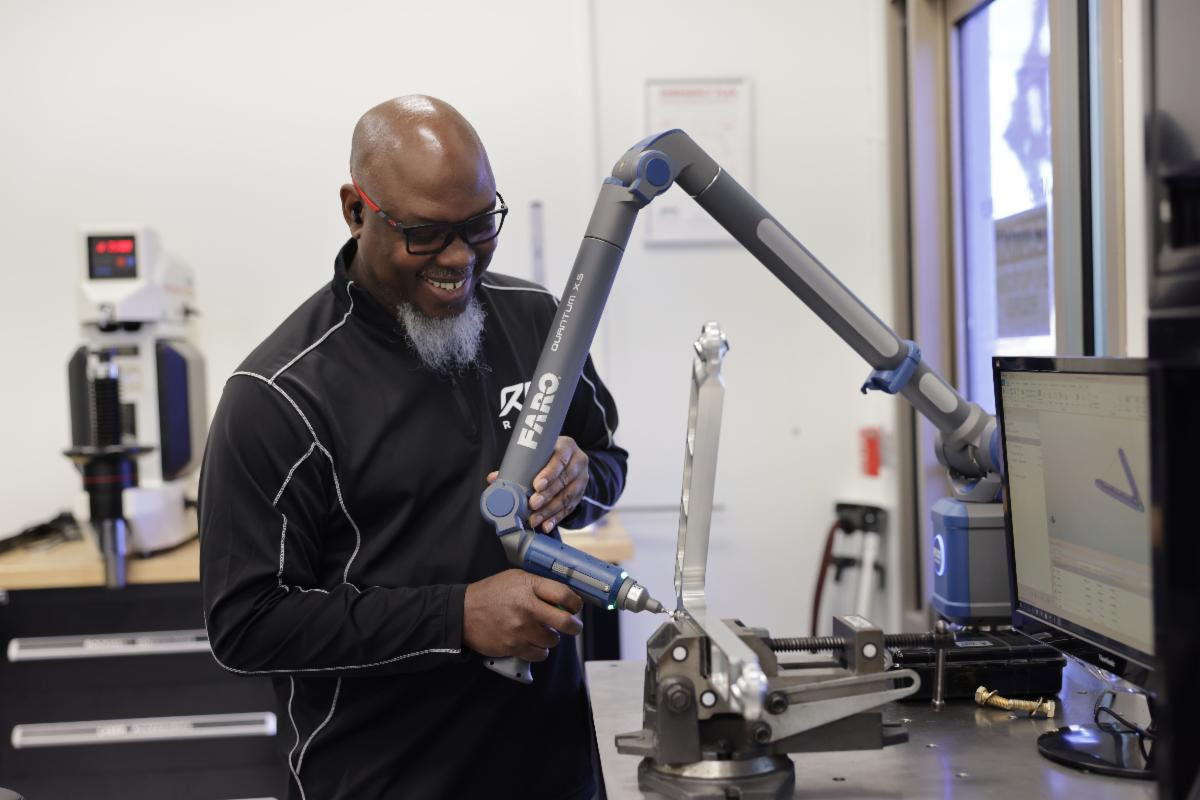 Man demonstrating a blue robotic arm in a laboratory setting with computer equipment