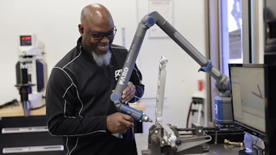 Man demonstrating a blue robotic arm in a laboratory setting with computer equipment