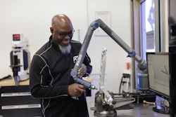 Man demonstrating a blue robotic arm in a laboratory setting with computer equipment