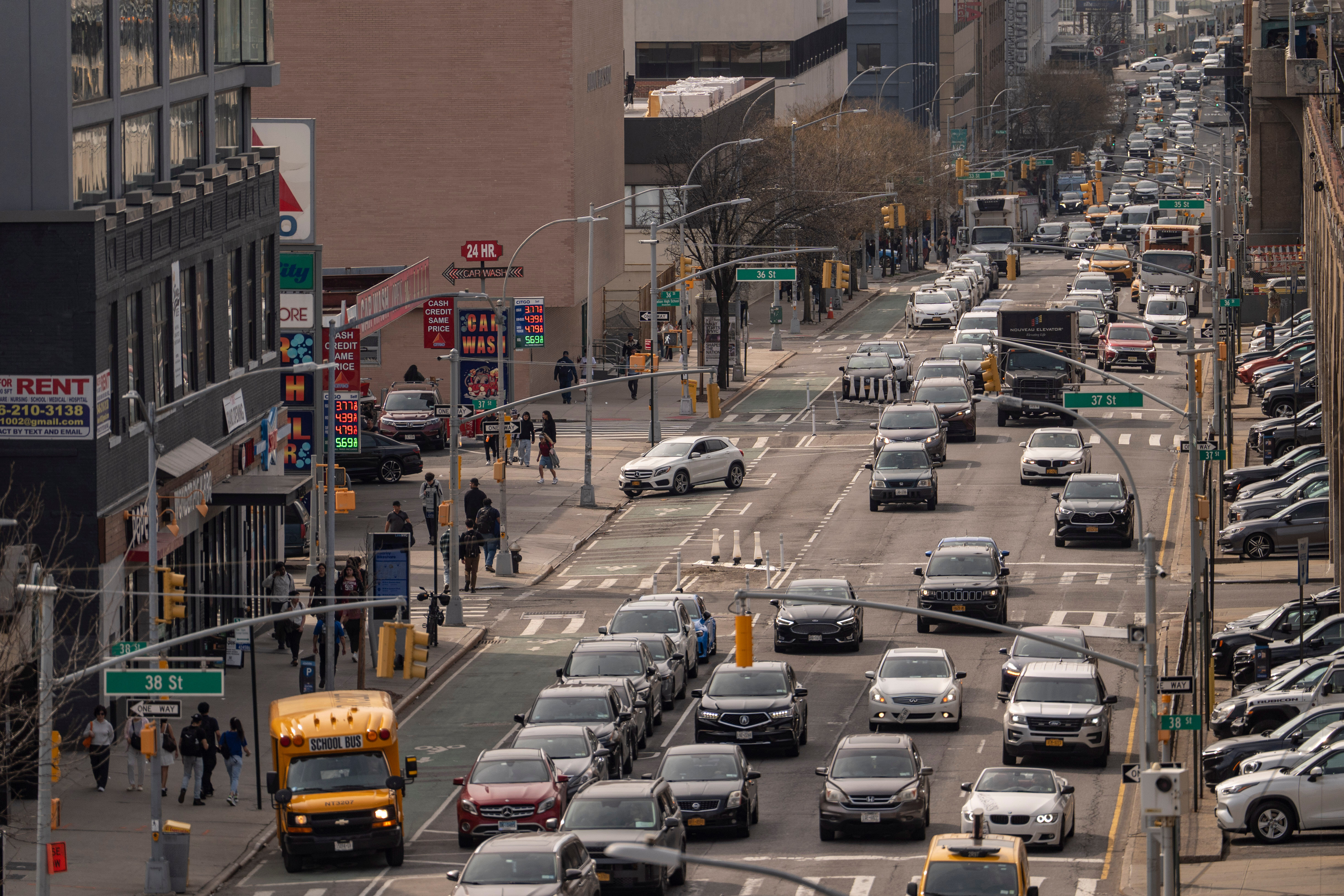 Busy urban intersection with heavy traffic, yellow taxi cabs, pedestrians, and commercial buildings in a major city street.