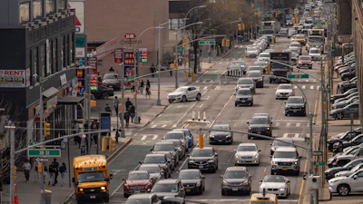 Busy urban intersection with heavy traffic, yellow taxi cabs, pedestrians, and commercial buildings in a major city street.