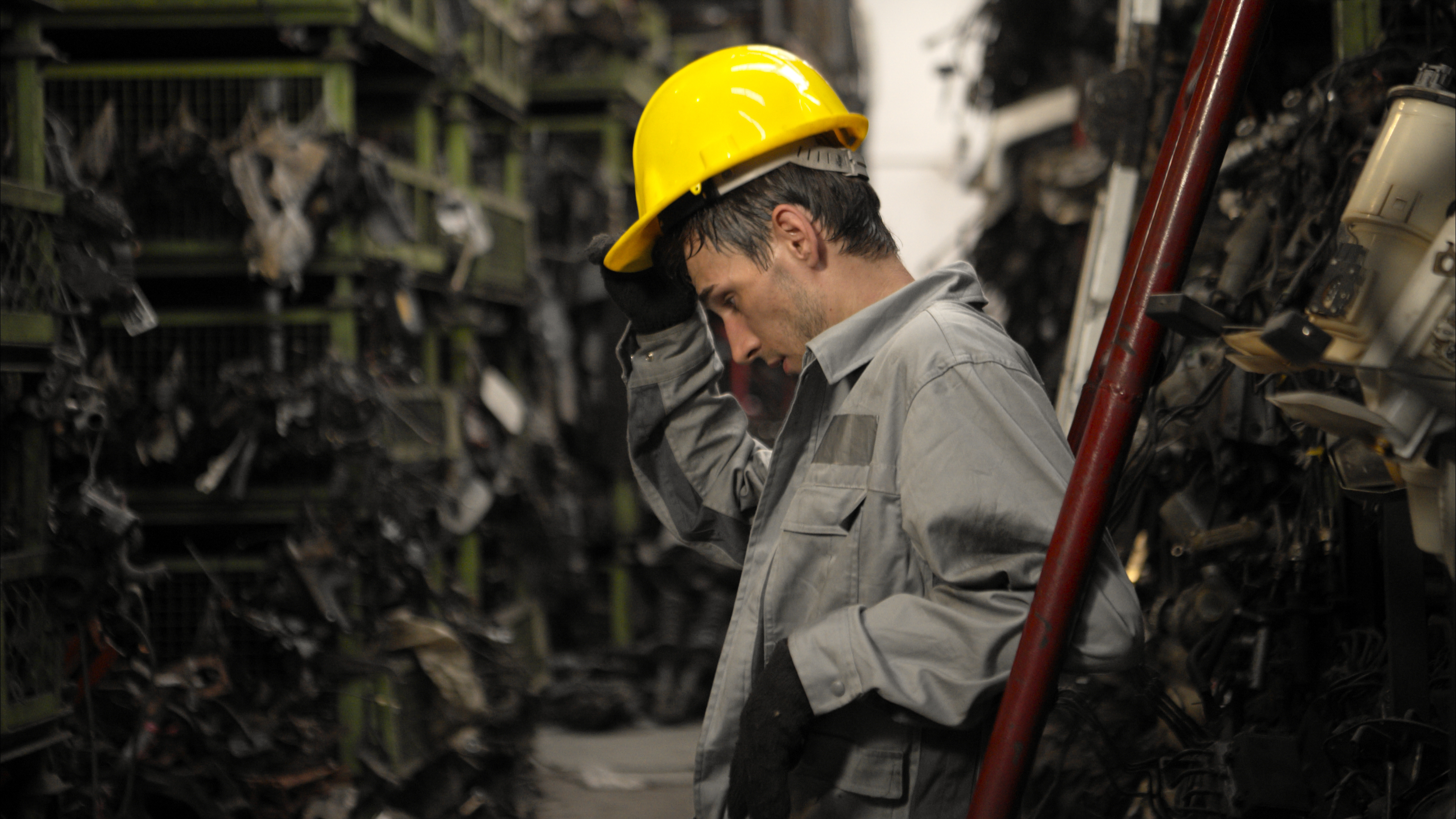 Industrial worker wearing yellow hard hat inspecting machinery in factory setting