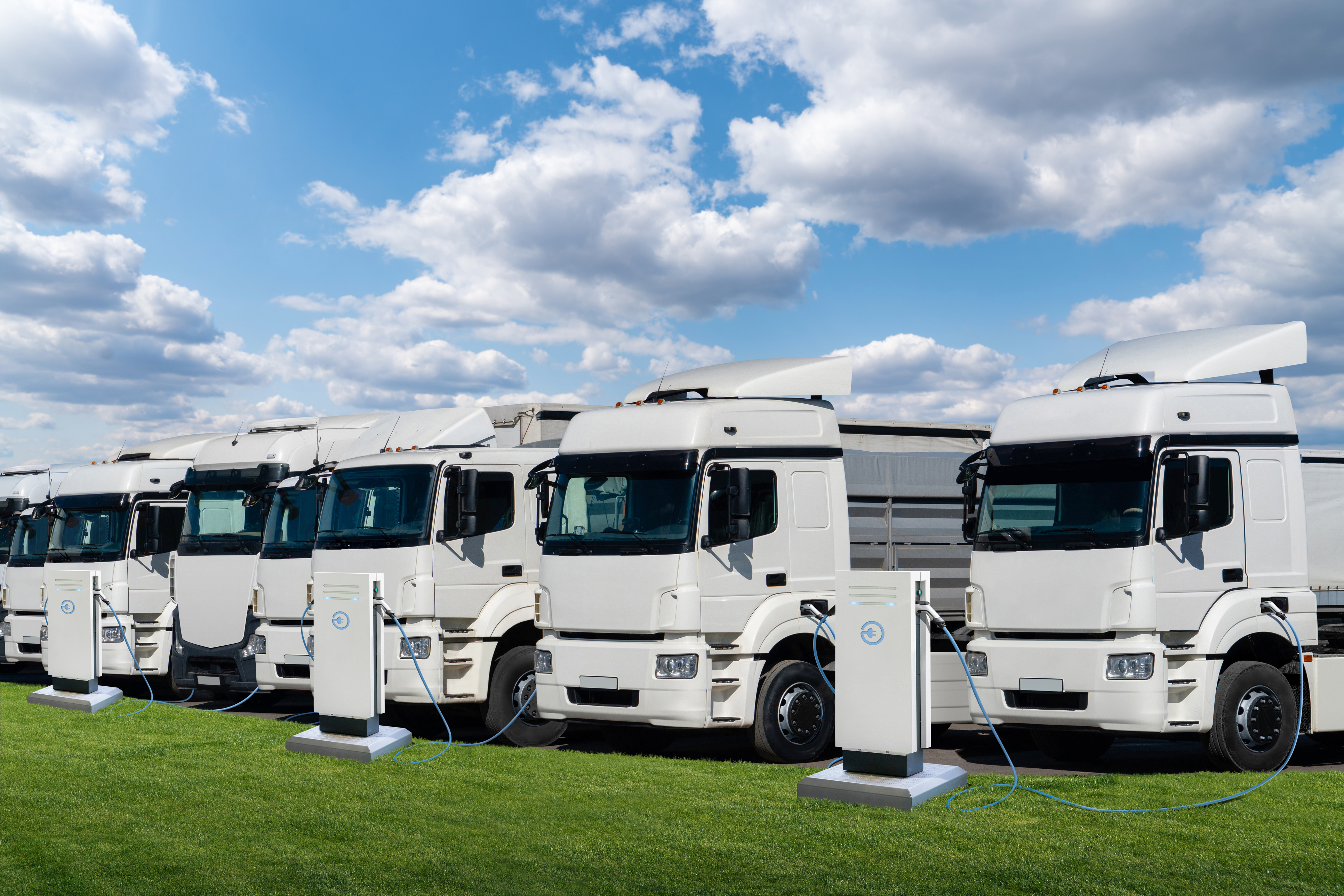 Fleet of white Renault electric trucks lined up on grass with charging cables