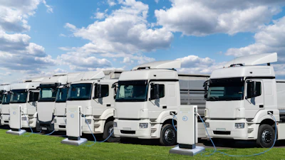 Fleet of white Renault electric trucks lined up on grass with charging cables