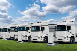 Fleet of white Renault electric trucks lined up on grass with charging cables