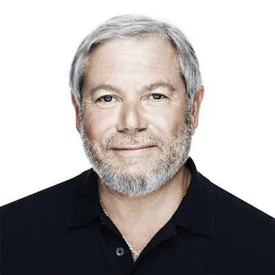 Professional headshot of a bearded man with gray hair wearing a black polo shirt