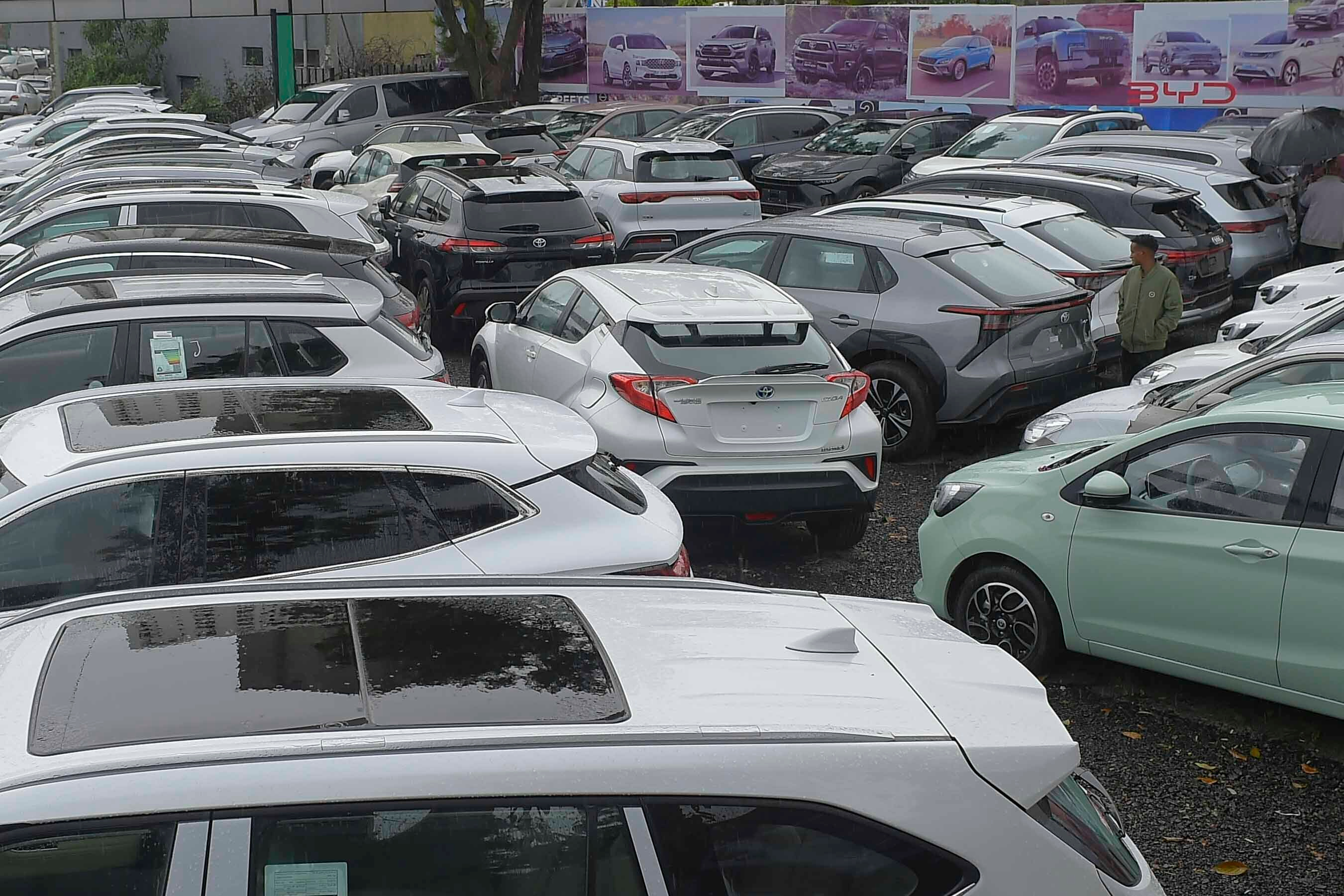 Used car dealership lot displaying multiple vehicles parked in rows with promotional banners in background