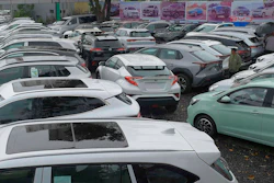 Used car dealership lot displaying multiple vehicles parked in rows with promotional banners in background