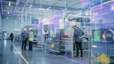 Modern factory floor with workers monitoring machinery and digital performance metrics displayed on transparent screens