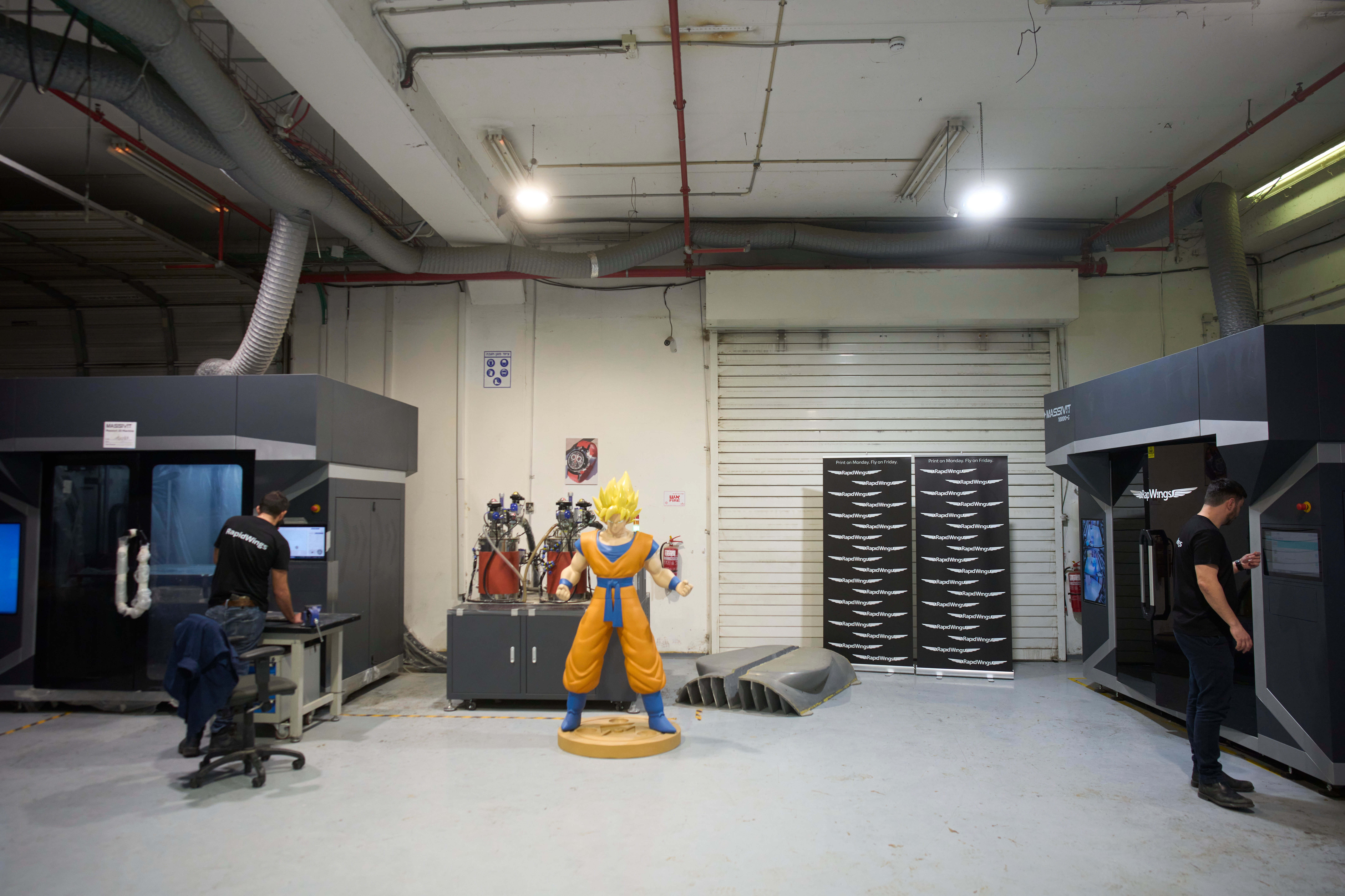 Industrial warehouse facility with yellow and blue anime character statue, workers, and manufacturing equipment