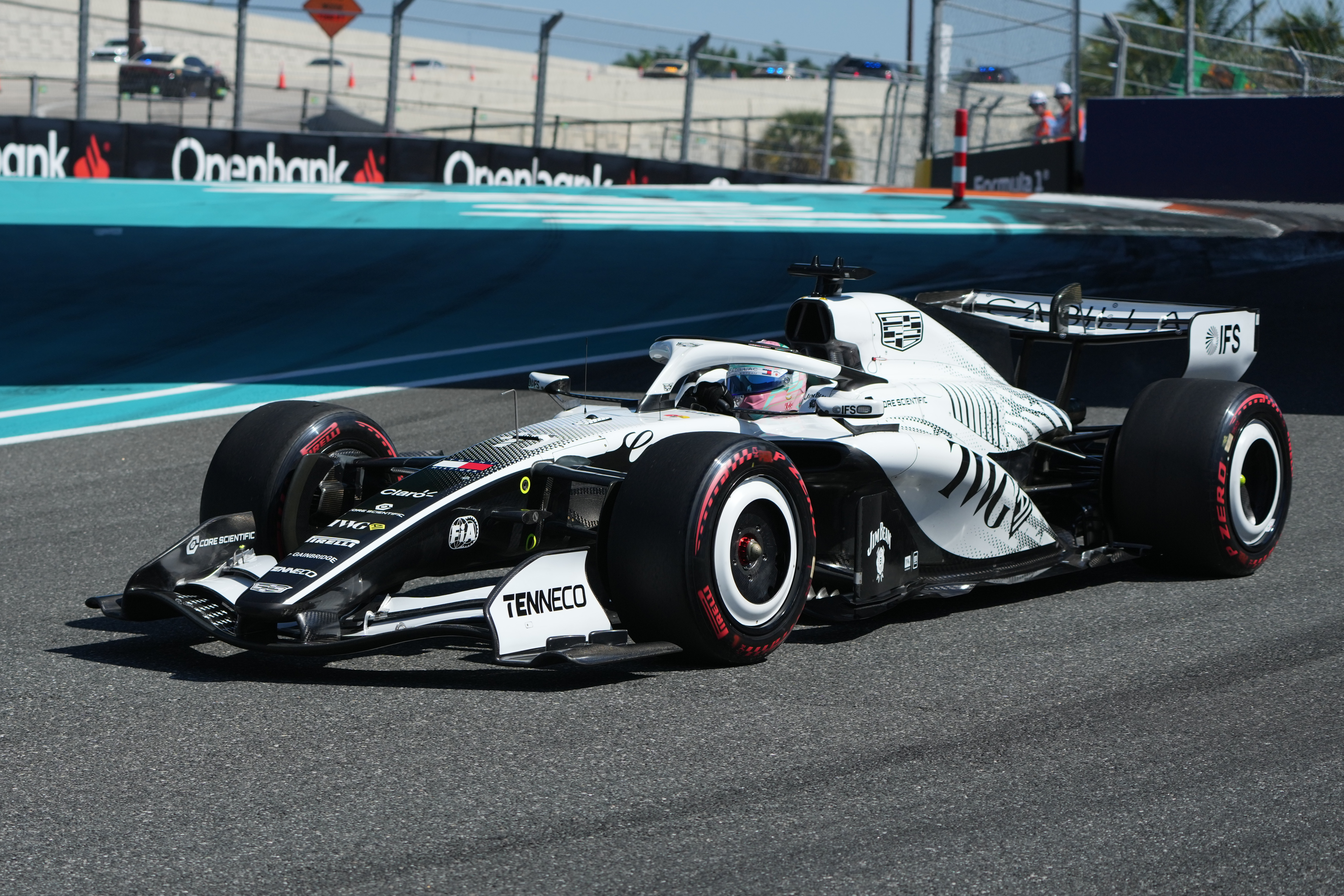 White and black Formula 1 racing car with red-trimmed tires on a circuit track with sponsor barriers