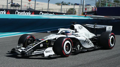 White and black Formula 1 racing car with red-trimmed tires on a circuit track with sponsor barriers