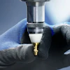 Plumber holding a brass pipe fitting with wrench and blue work gloves