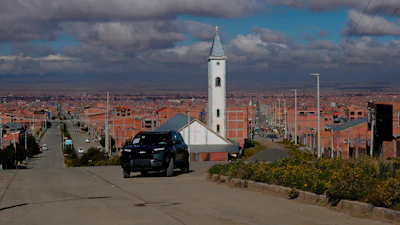 White church with tall steeple on hillside overlooking sprawling city with orange-brick buildings under cloudy sky