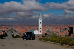 White church with tall steeple on hillside overlooking sprawling city with orange-brick buildings under cloudy sky