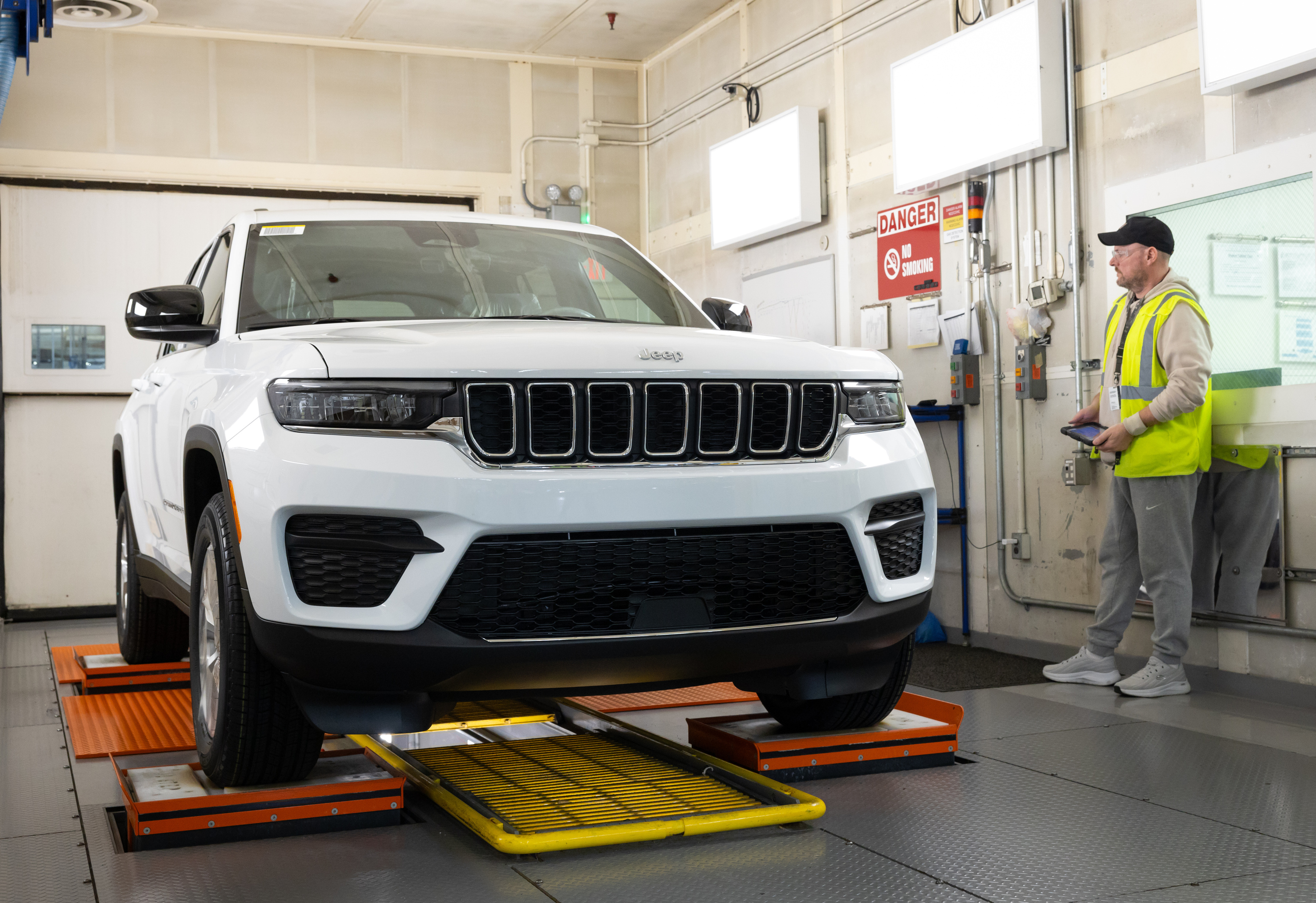 White Jeep Grand Cherokee on alignment equipment in automotive service bay with technician