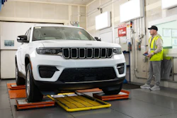 White Jeep Grand Cherokee on alignment equipment in automotive service bay with technician