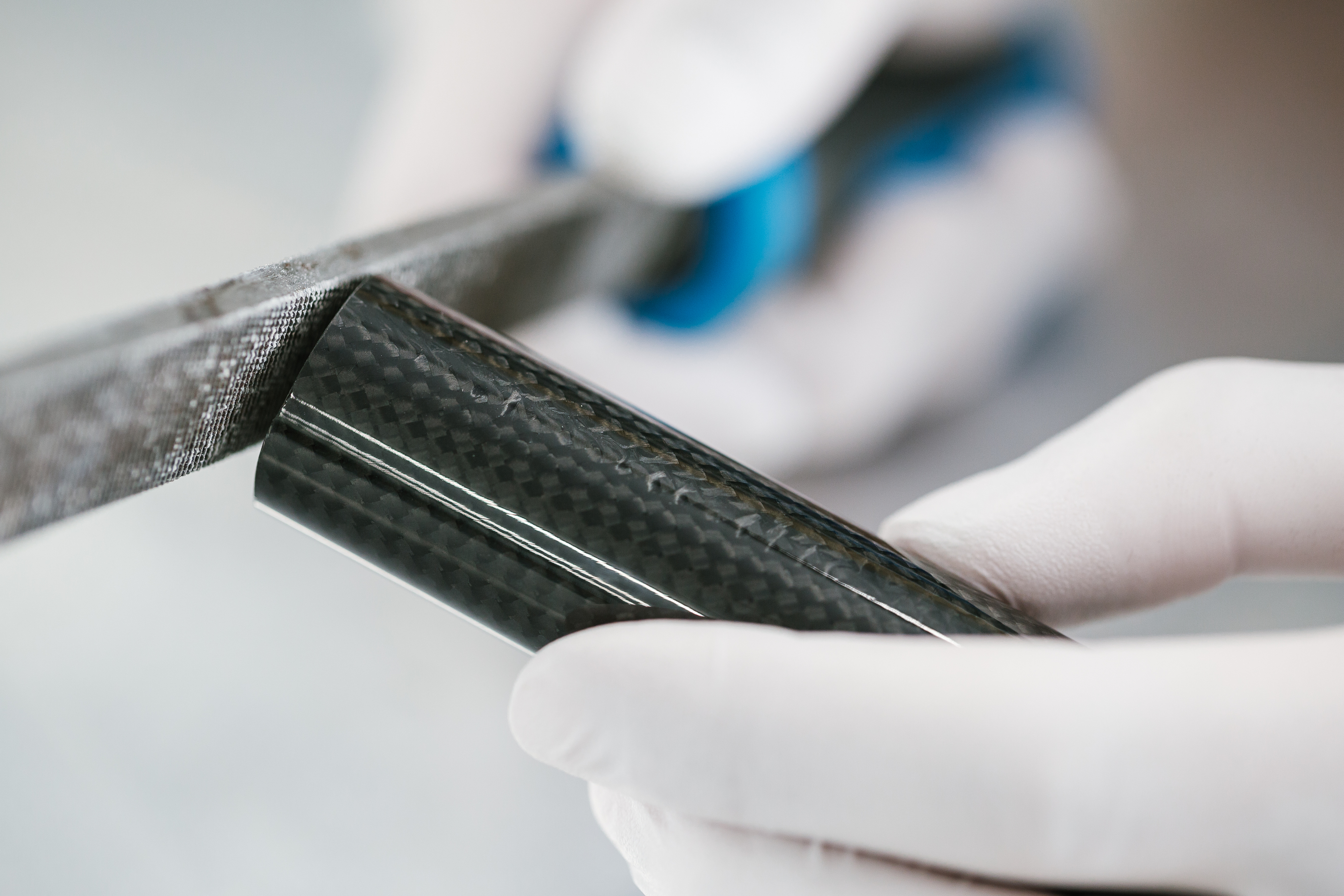 Close-up of carbon fiber material sample held in white gloved hands during inspection