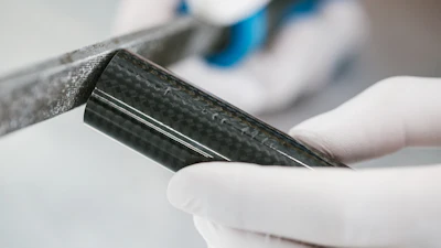Close-up of carbon fiber material sample held in white gloved hands during inspection