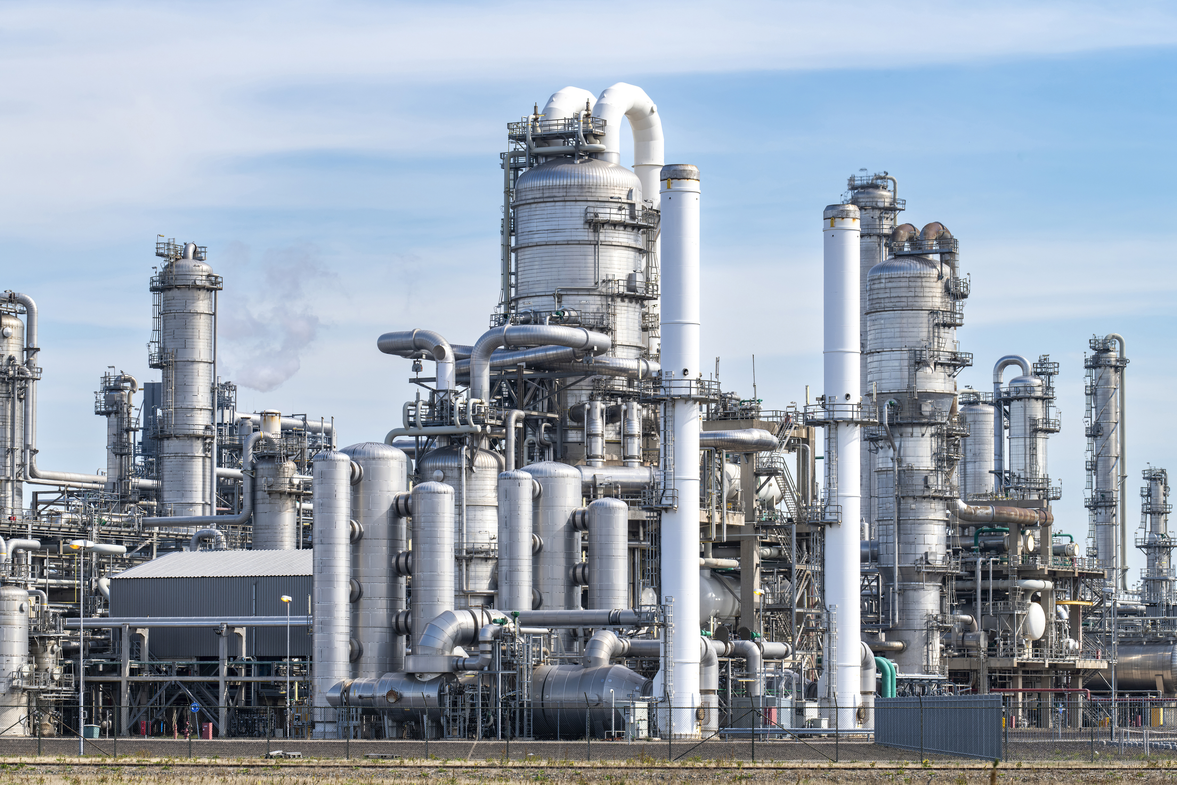 Large petrochemical refinery complex with multiple distillation towers, cylindrical vessels, and interconnected piping systems under clear blue sky