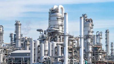 Large petrochemical refinery complex with multiple distillation towers, cylindrical vessels, and interconnected piping systems under clear blue sky