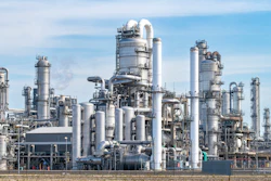 Large petrochemical refinery complex with multiple distillation towers, cylindrical vessels, and interconnected piping systems under clear blue sky