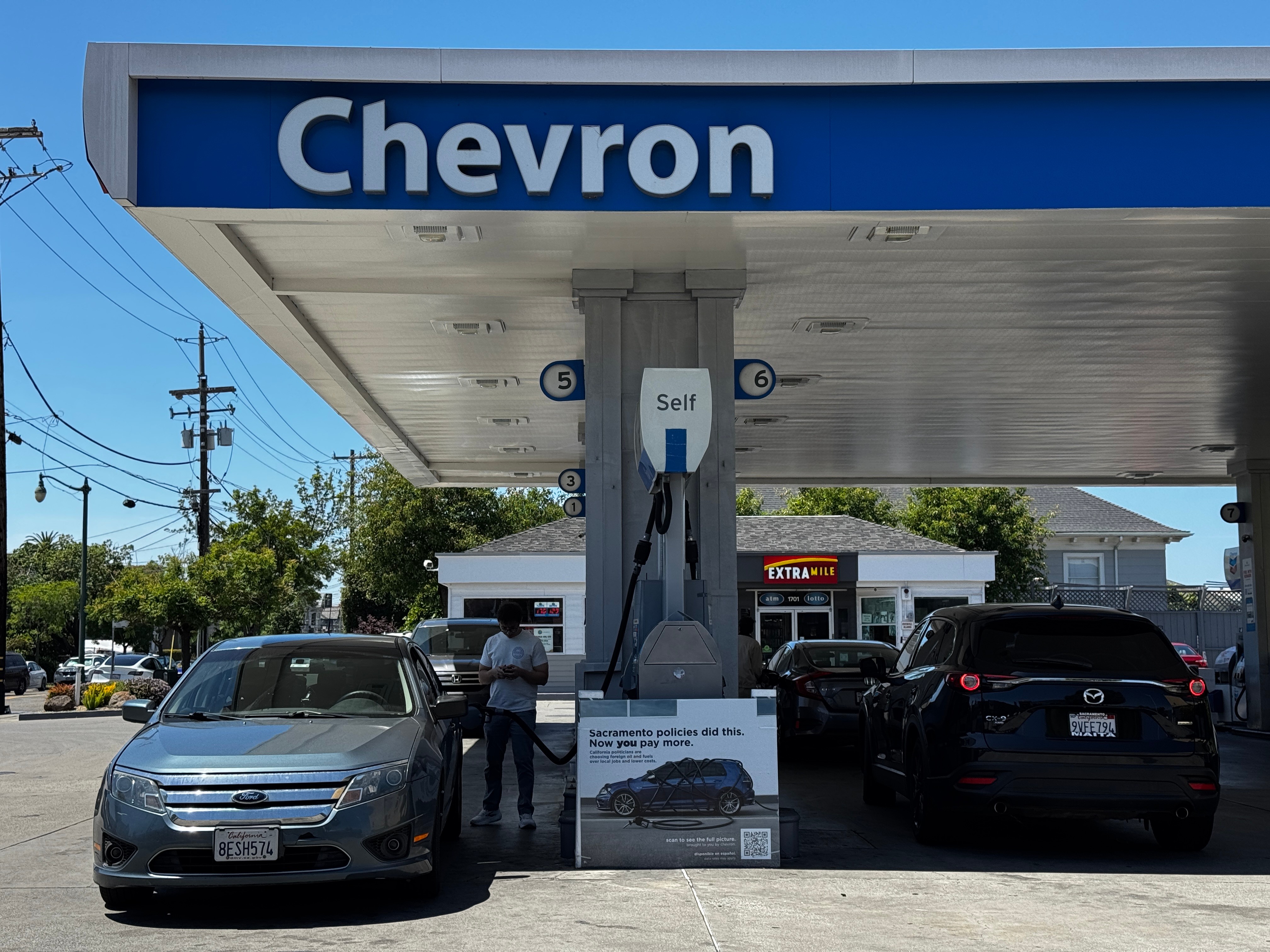 Chevron gas station with self-service fuel pumps and parked vehicles under blue canopy