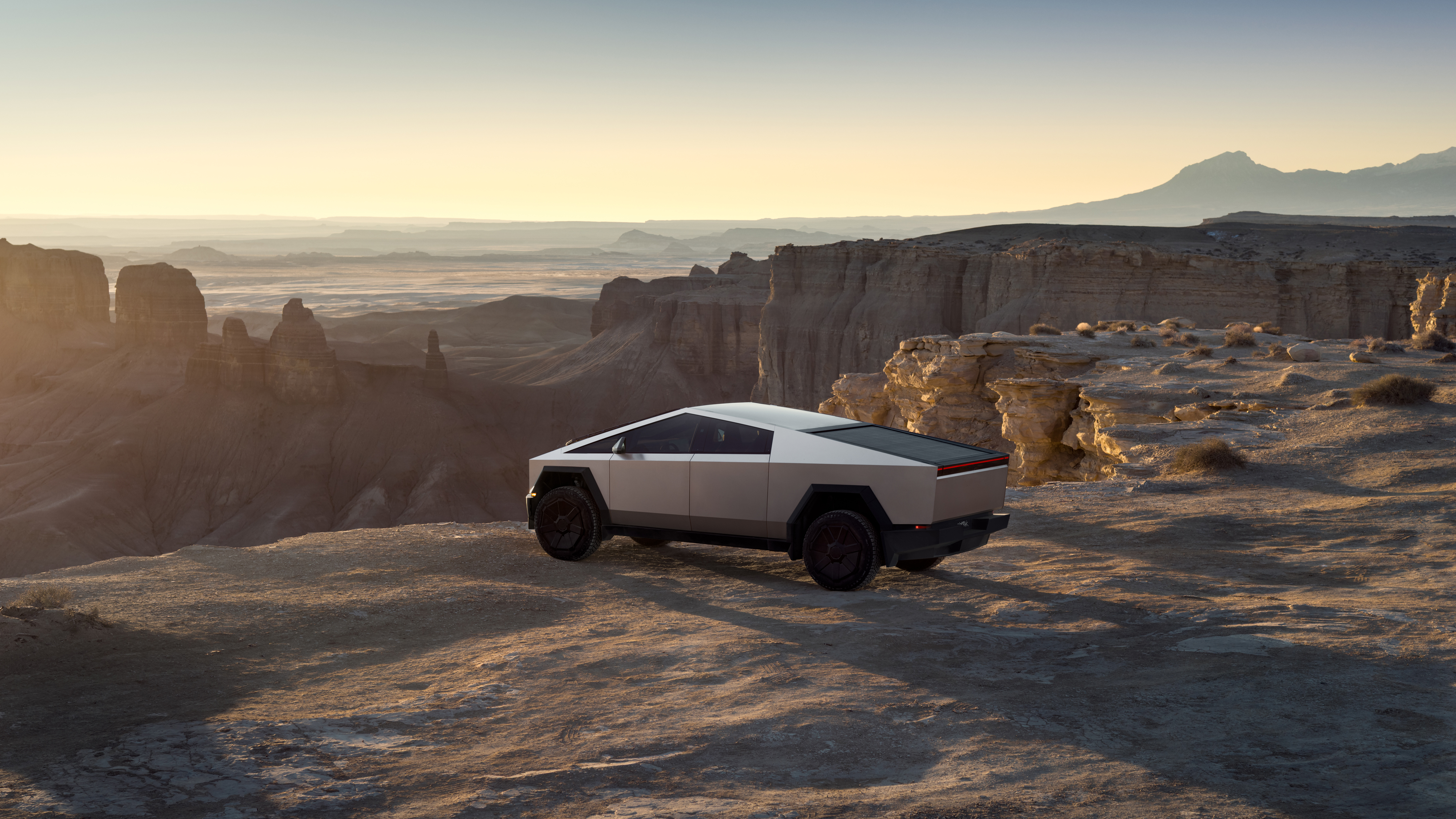Tesla Cybertruck parked on desert plateau with rock formations and mountains at sunset