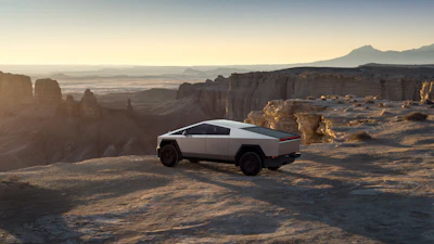 Tesla Cybertruck parked on desert plateau with rock formations and mountains at sunset