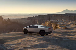 Tesla Cybertruck parked on desert plateau with rock formations and mountains at sunset