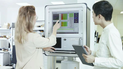 Two professionals examine data on a laboratory analysis system with color-coded results displayed on the monitor.