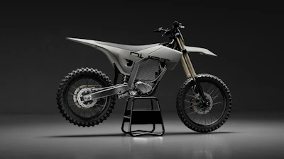 Modern electric dirt bike with white bodywork and dual disc brakes displayed on black stand