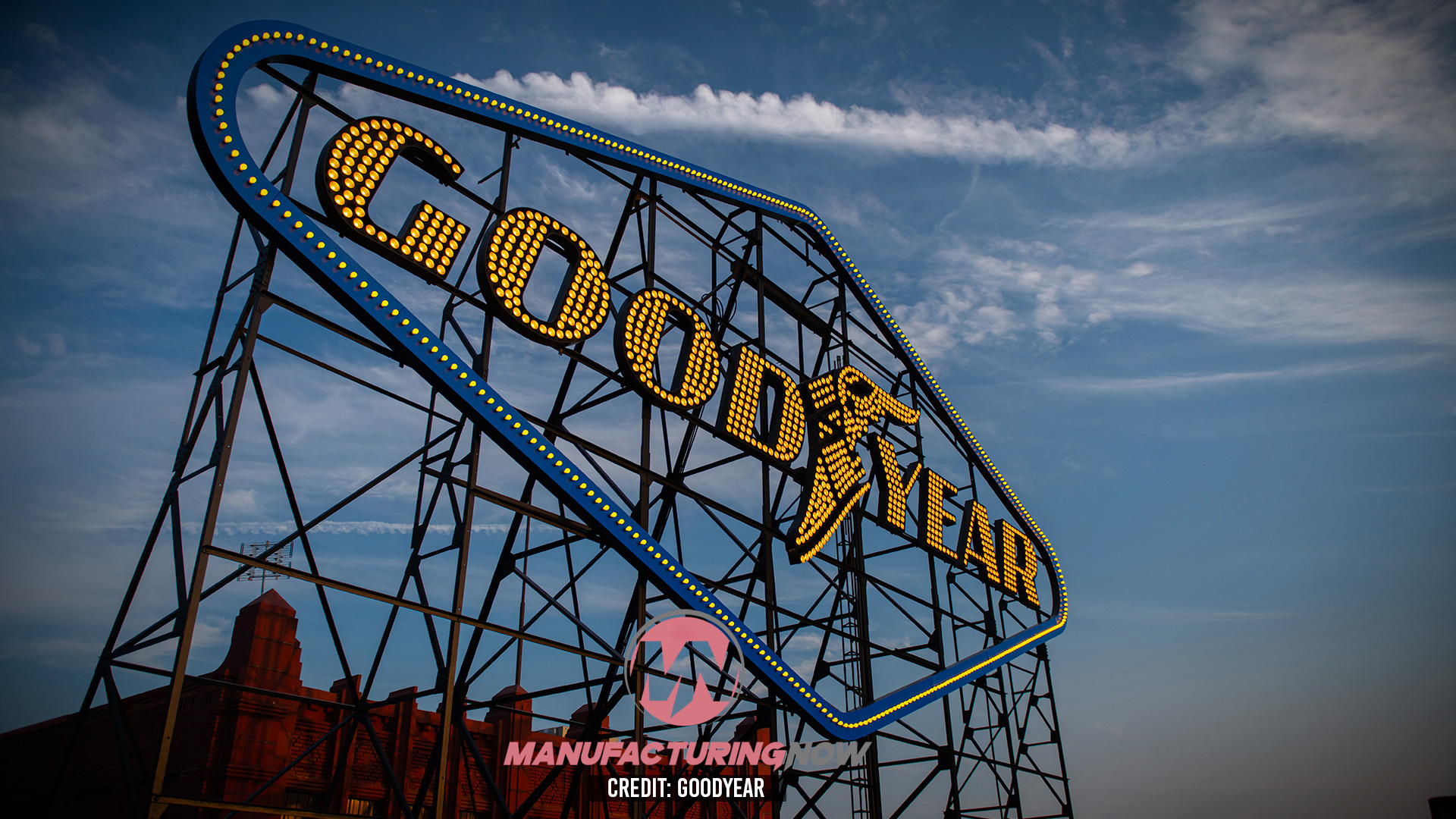 Vintage Goodyear neon sign with yellow lettering and blue trim against a cloudy sky