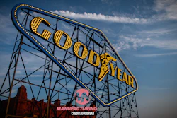 Vintage Goodyear neon sign with yellow lettering and blue trim against a cloudy sky