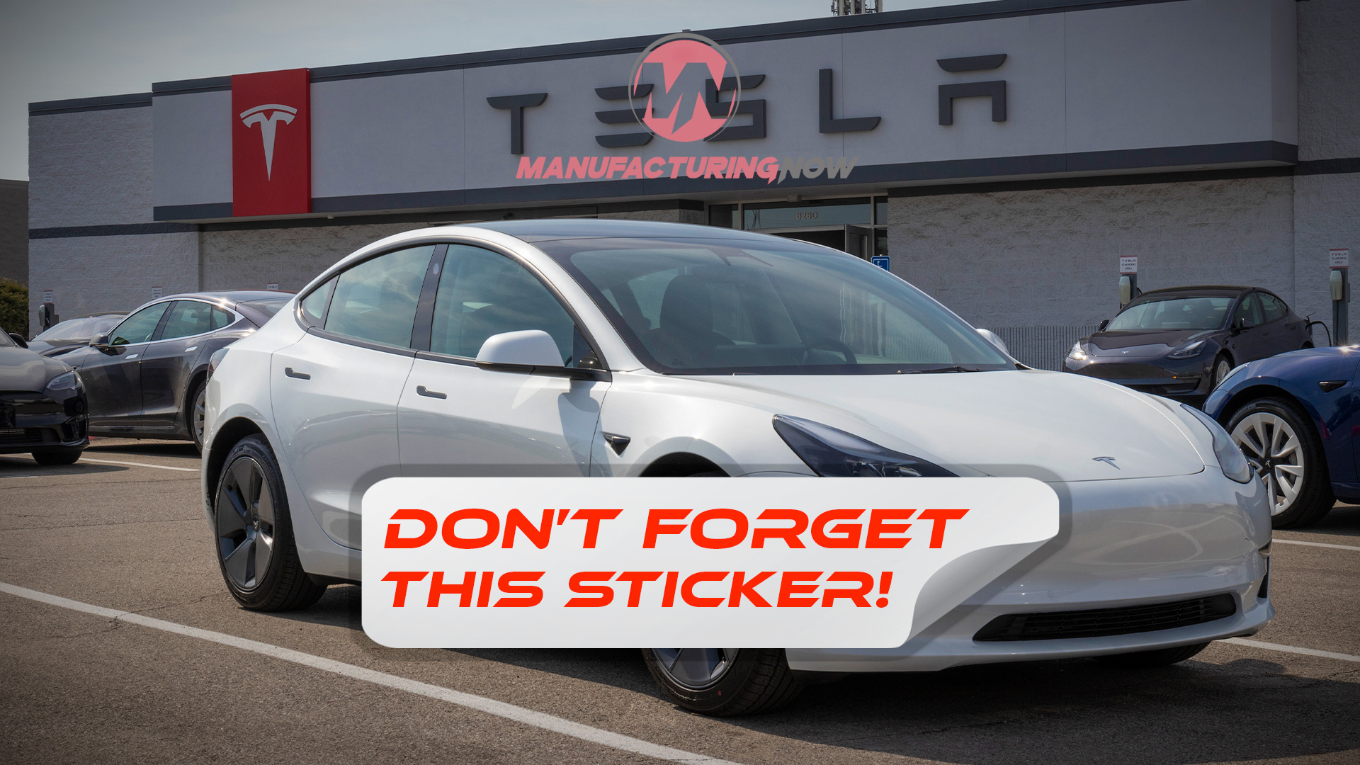 White Tesla sedan parked at Tesla manufacturing facility with company signage visible