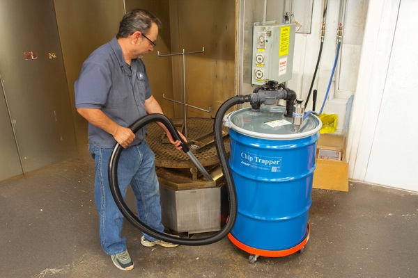 Technician operating a blue Chip Trapper dust collection system in a workshop setting