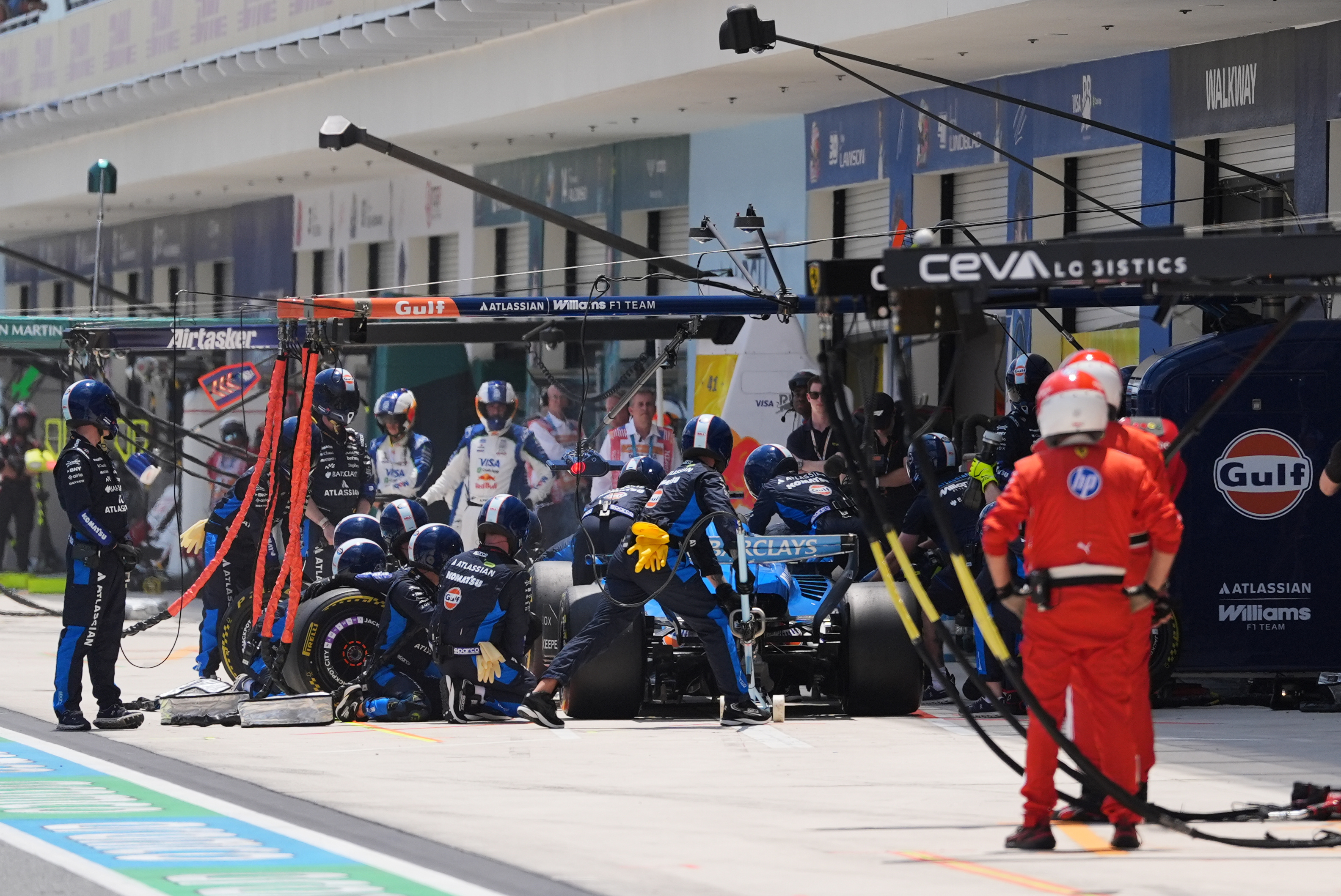 Formula 1 pit crew performing a tire change during a race stop with team members in red and blue uniforms working on a race car.