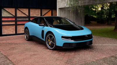 Bright blue Lotus Emira sports car parked on brick driveway beside Tudor-style building