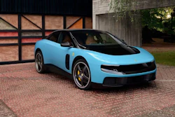 Bright blue Lotus Emira sports car parked on brick driveway beside Tudor-style building