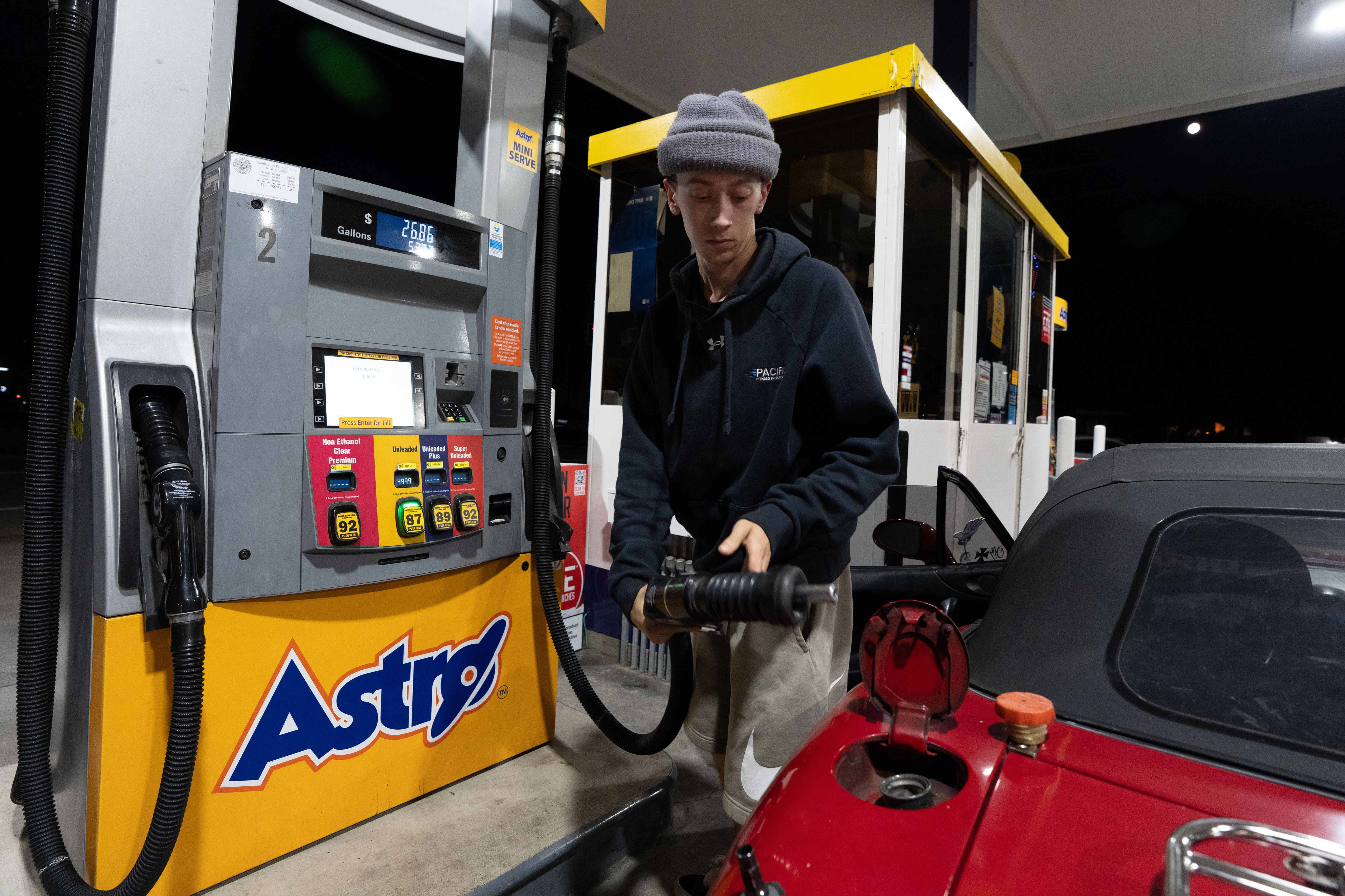 Person refueling red car at Astro gas station pump at night